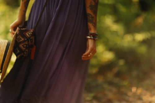 Free A woman in a flowing purple dress with bracelets walks holding a hat, exuding bohemian style. Stock Photo