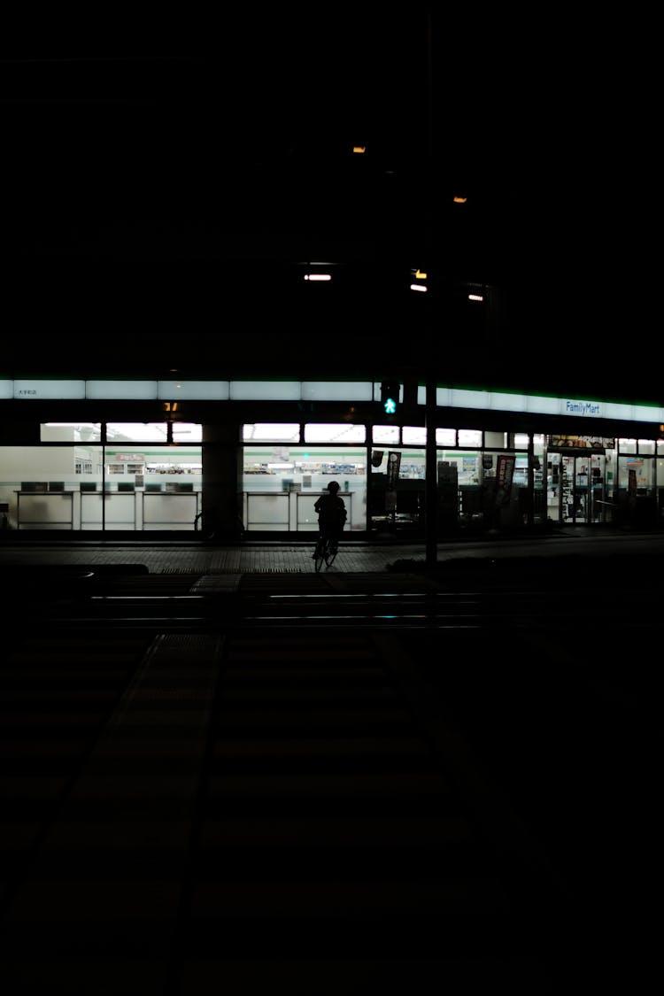 Silhouette Of A Person Biking On Sidewalk At Night