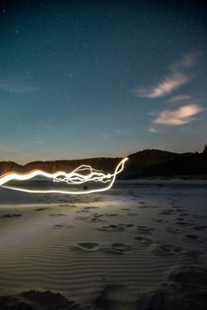 Ethereal light trails illuminate a tranquil beach under a star-studded night sky, creating a blend of nature and art.