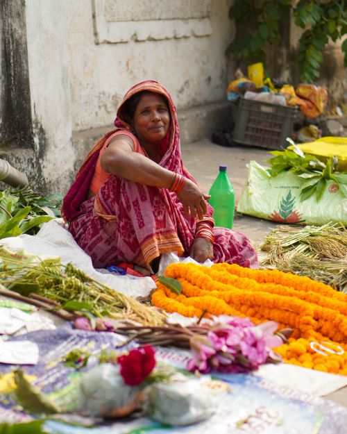 Free A woman vendor at a street market sells vibrant flowers, sitting amidst her colorful display. Stock Photo