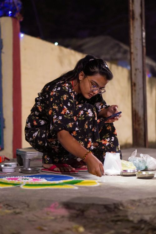 Free A woman skillfully creates colorful Rangoli designs in India, surrounded by vibrant powders and materials at night. Stock Photo