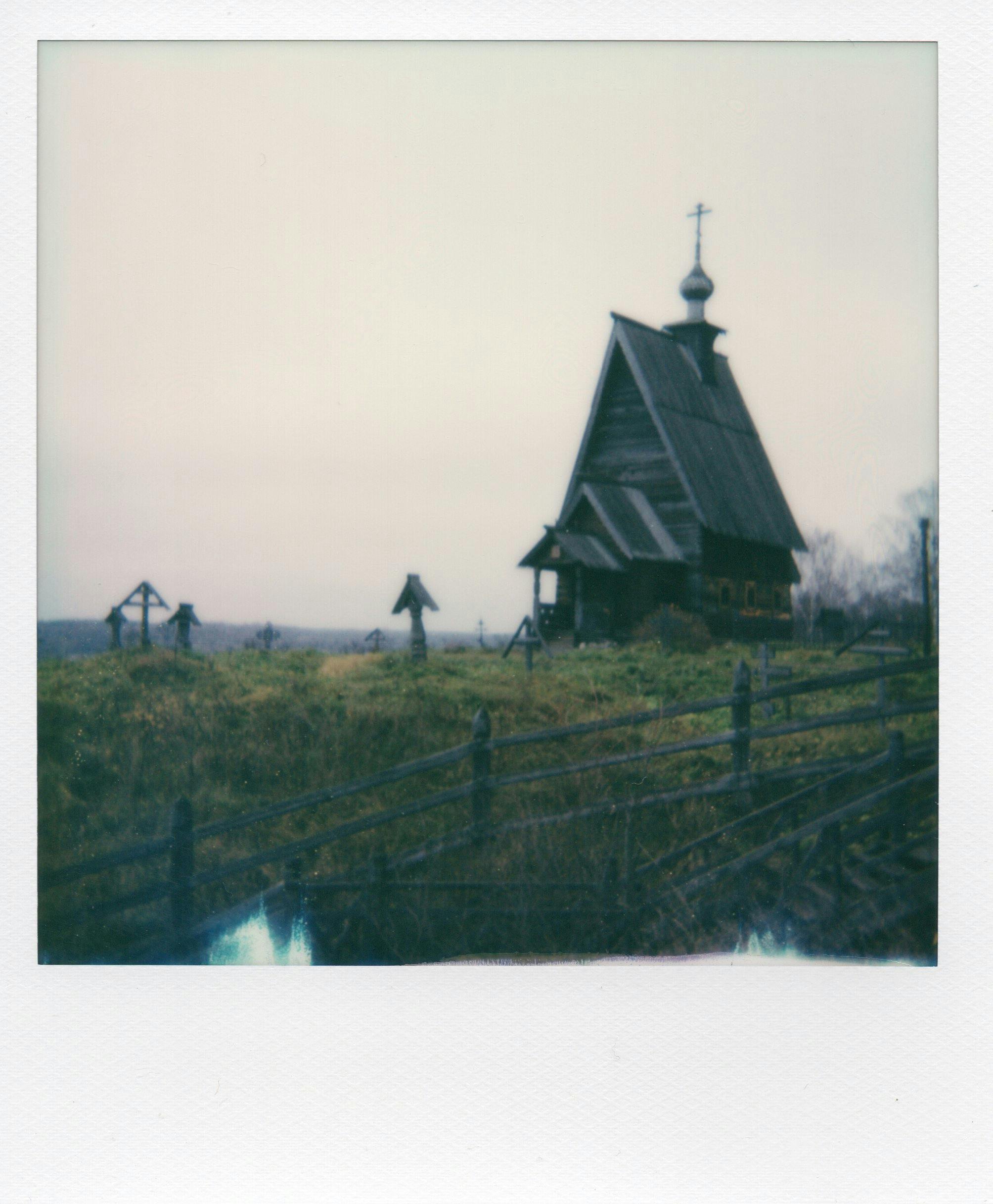 Vintage-style Polaroid of an old wooden church in Ples, Russia, amidst a serene rural landscape.