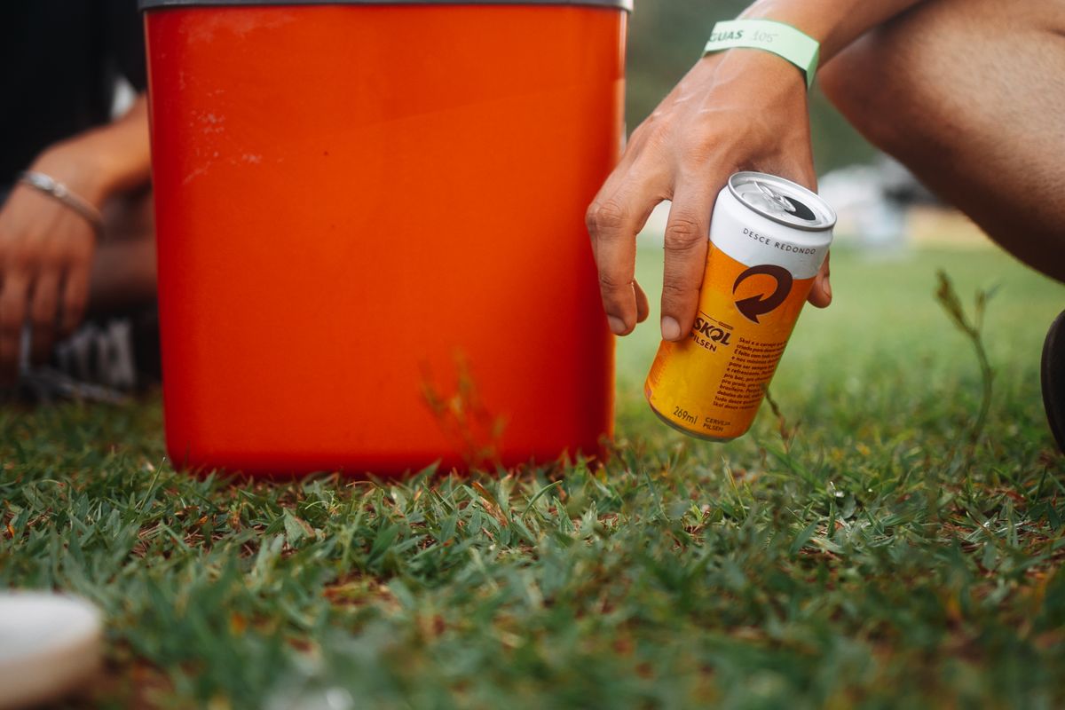 Hand reaching for a cold drink beside a bright orange cooler on the grass at a tailgate