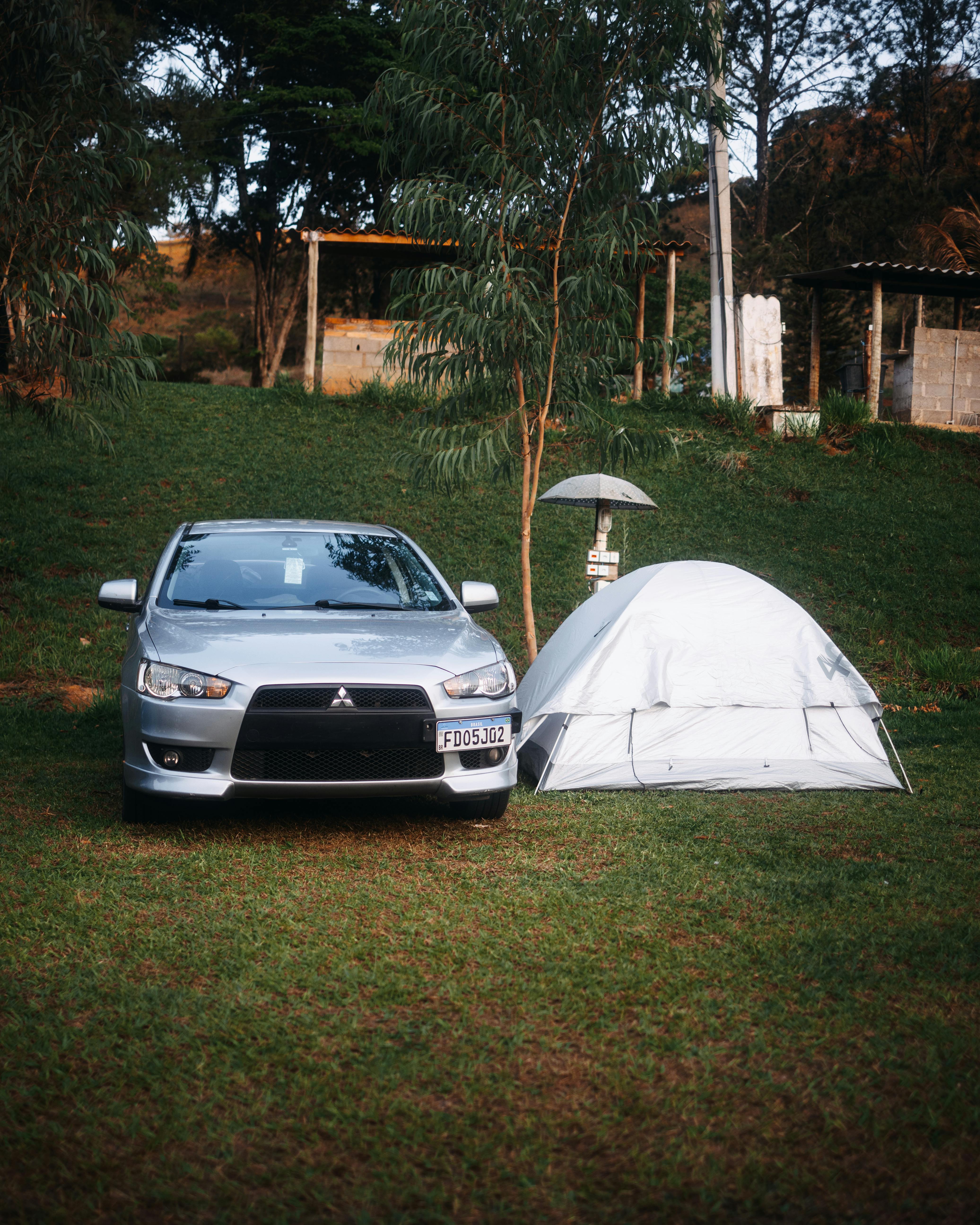 A serene campsite featuring a Mitsubishi Lancer beside a white tent on a grassy field.