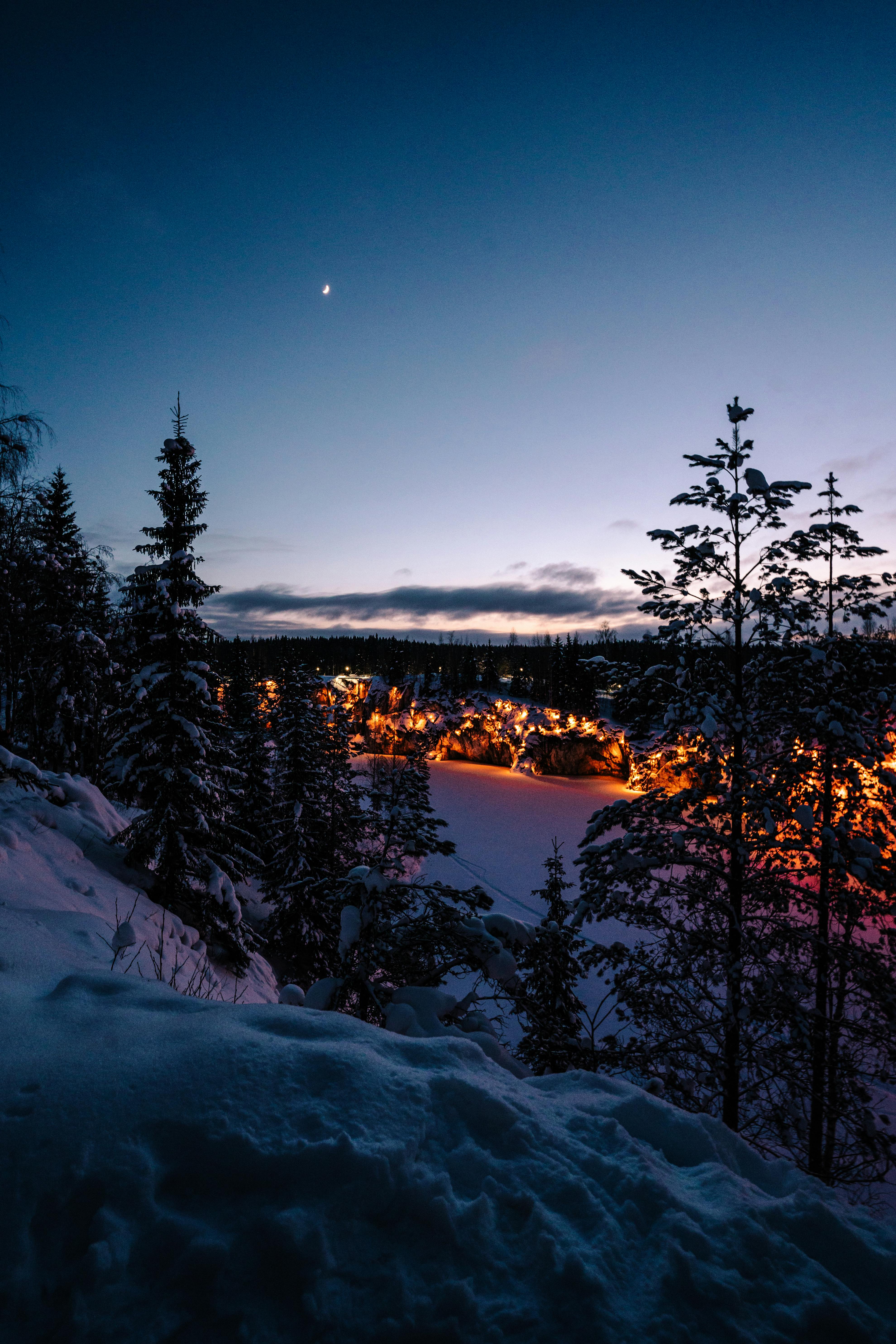Captivating view of a snowy village illuminated at twilight with a crescent moon above.