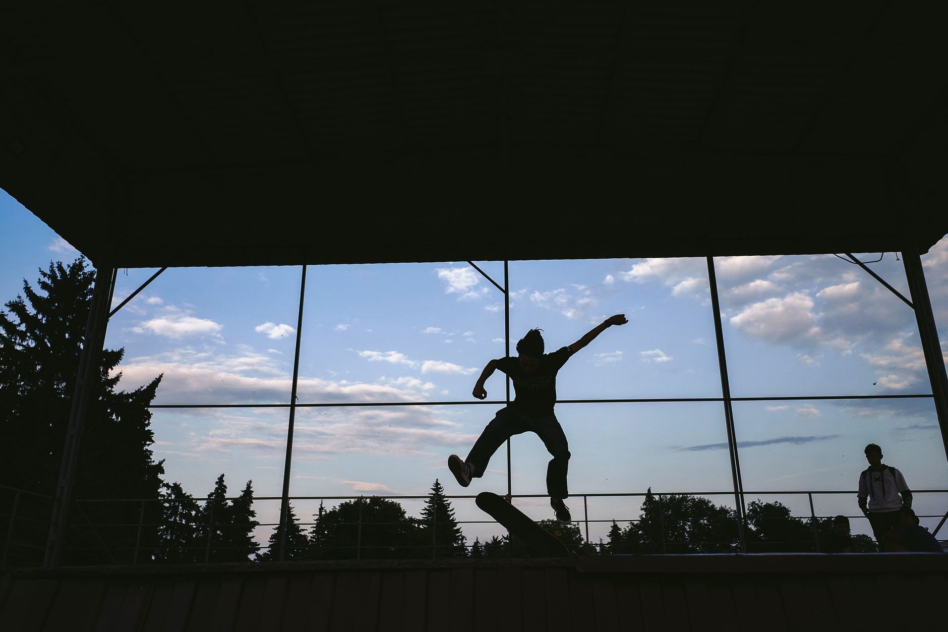 Silhouette of a skateboarder executing a trick mid-air with a vibrant blue sky backdrop.. silhouette, skateboarder, executing