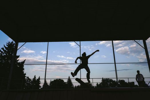 Silhouette of a skateboarder executing a trick mid-air with a vibrant blue sky backdrop.. silhouette, skateboarder, executing