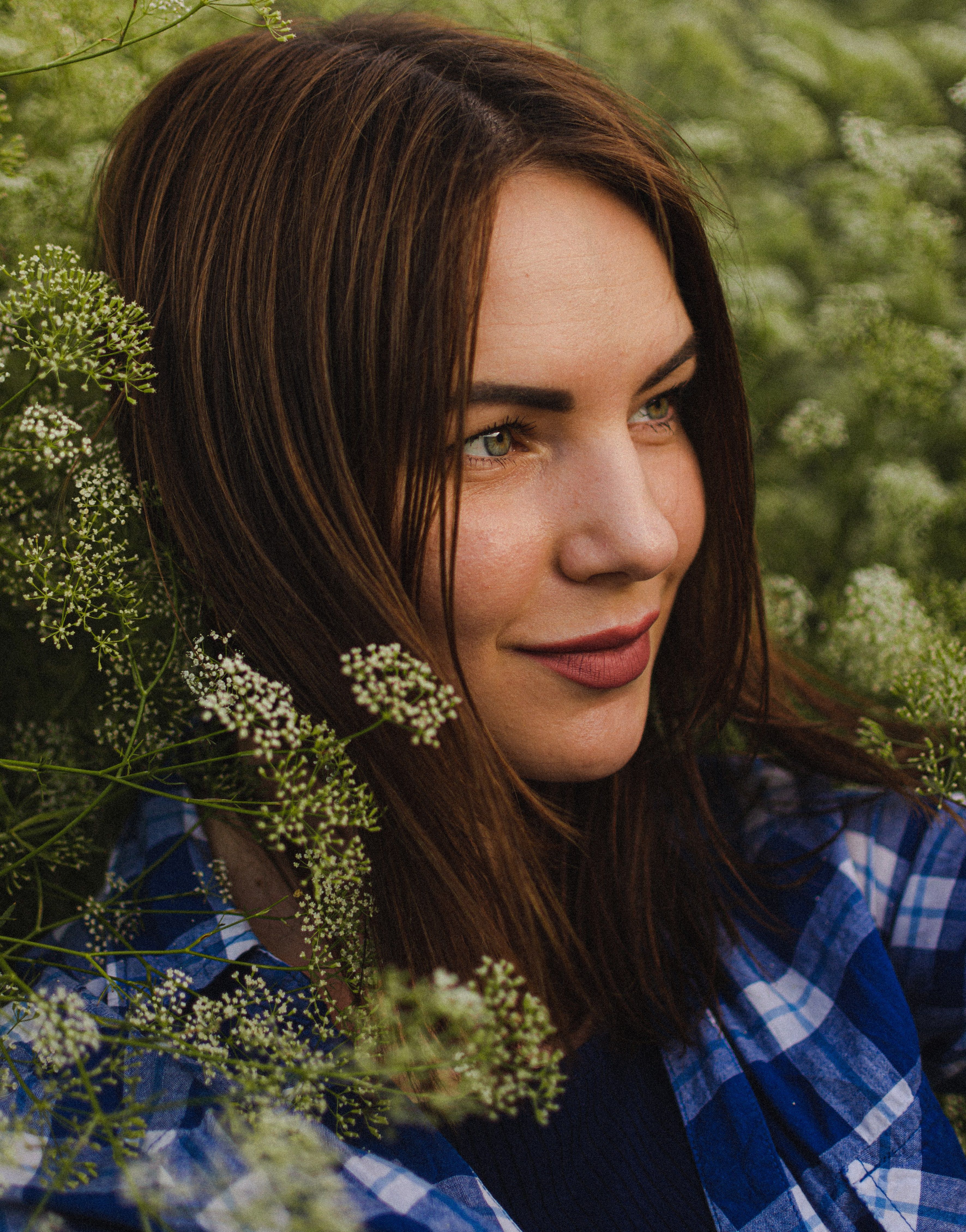Portrait of a young woman smiling among white flowers outdoors.