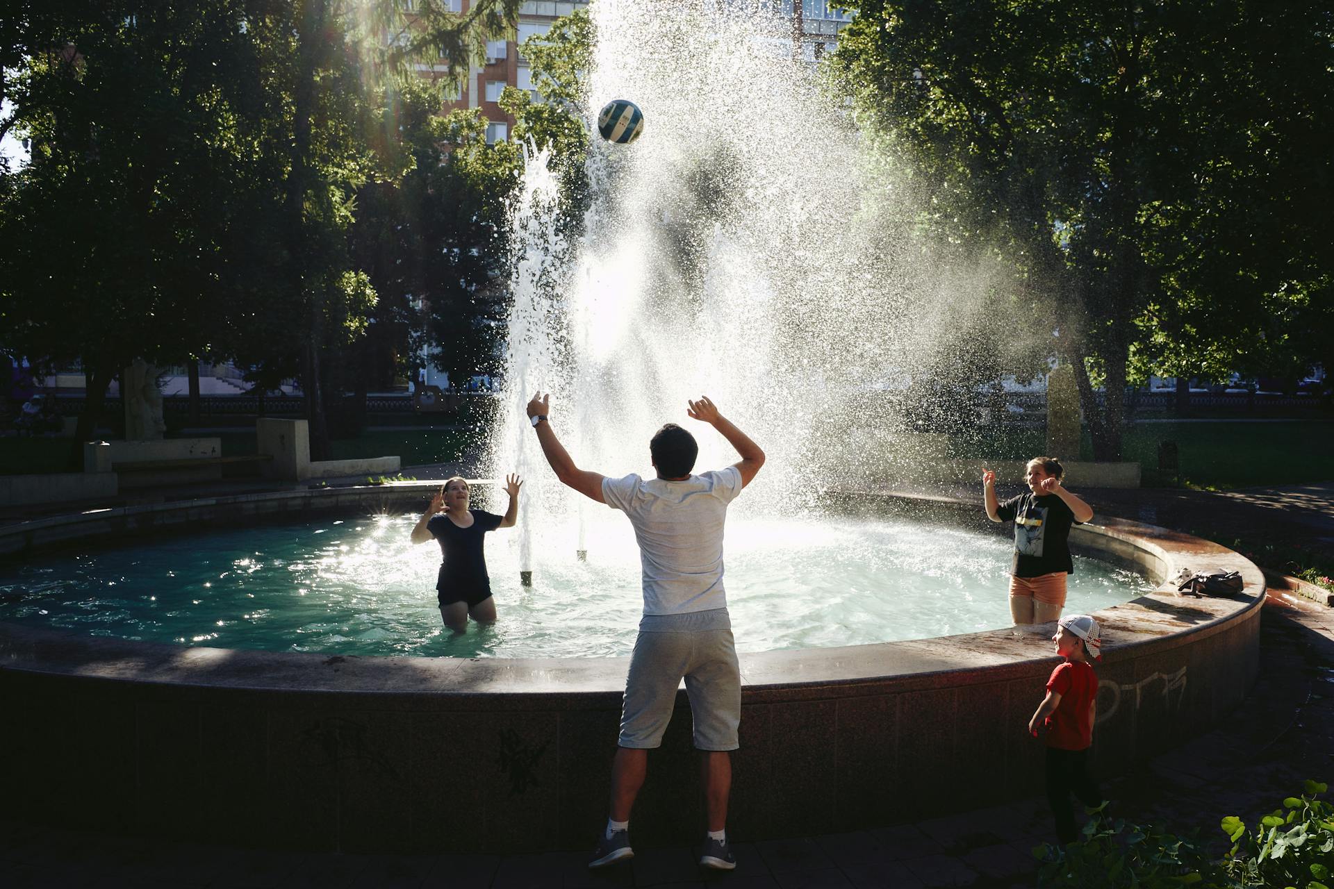 A joyful outdoor play session with a family enjoying a water fountain splash in the park.