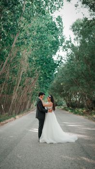 A newlywed couple embraces on a scenic tree-lined road, capturing a romantic moment.