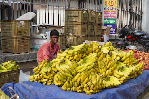 A local vendor with a banana stand in an outdoor Indian market, with fresh produce on display.