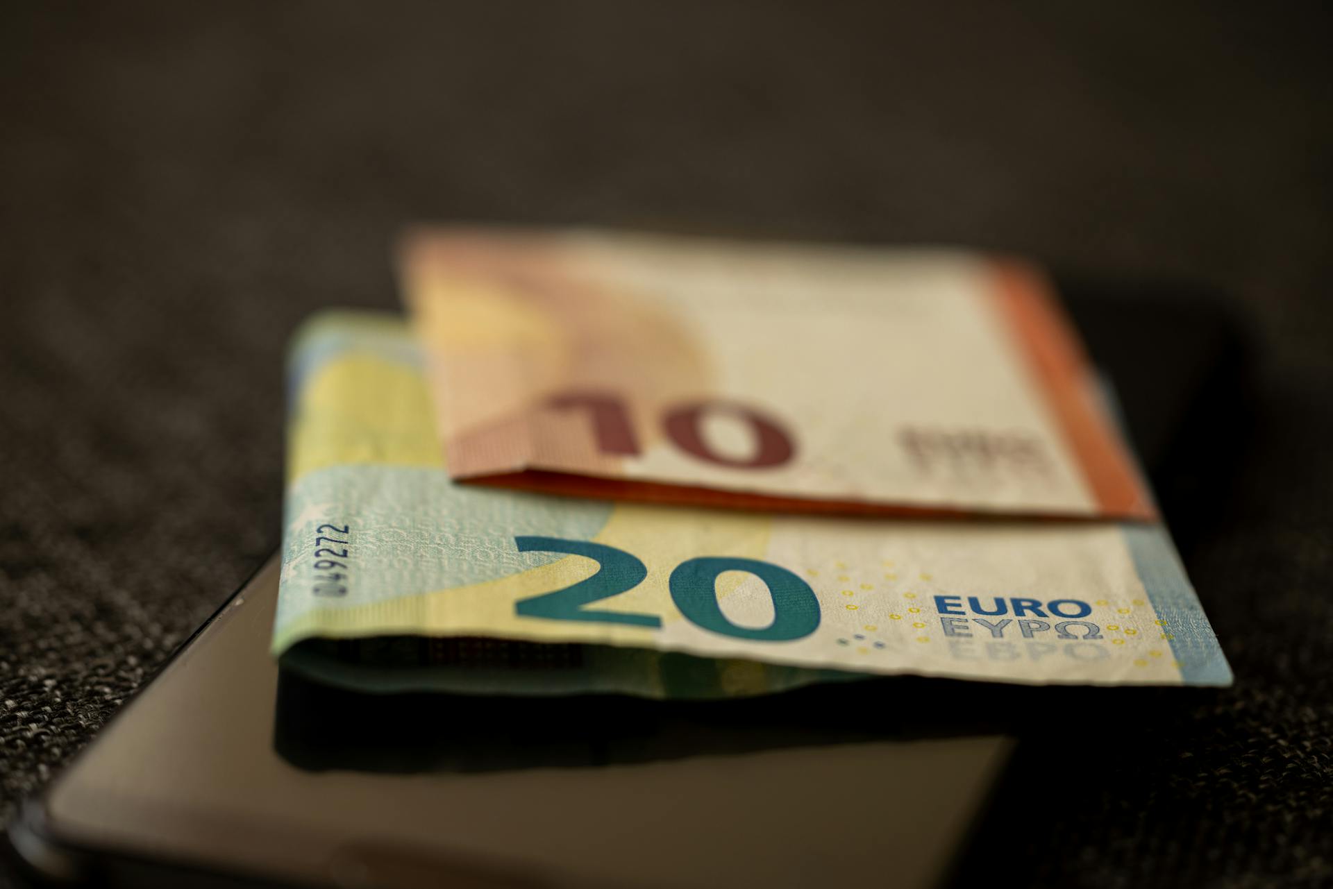 A detailed close-up shot of 10 and 20 euro banknotes placed on a smartphone, representing finance and technology.