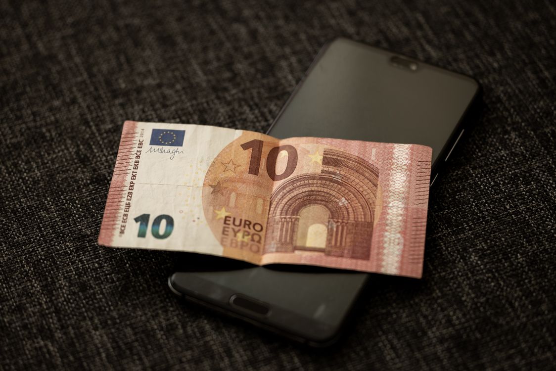 Euro novčanica položena na zaslon pametnog telefona, simbolizirajući spoj fizičkog novca i digitalne tehnologije