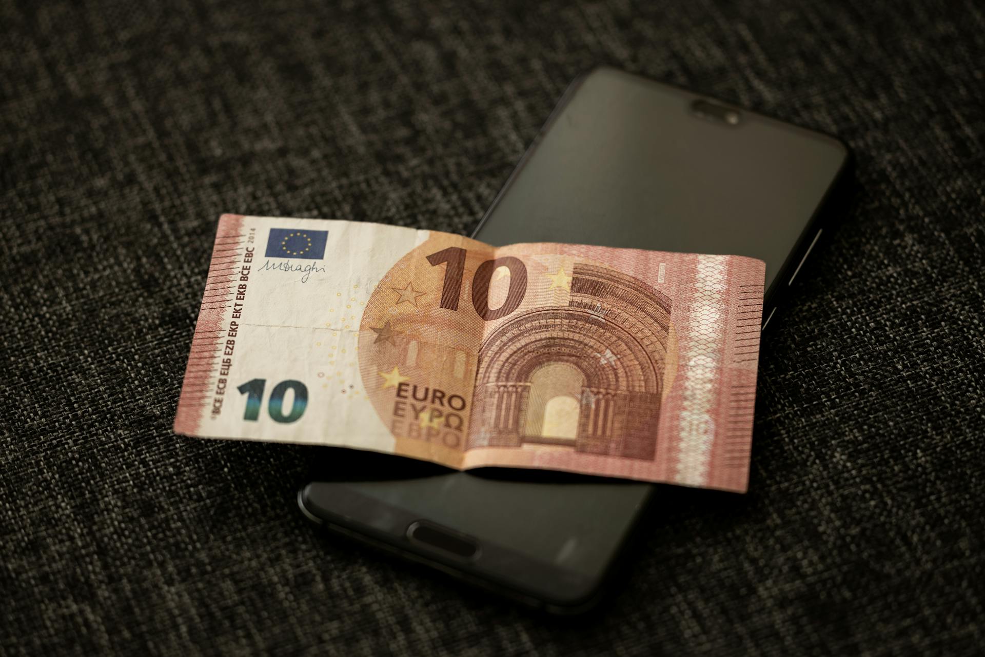 A close-up shot of a 10 euro banknote placed on a smartphone, highlighting currency and digital technology.