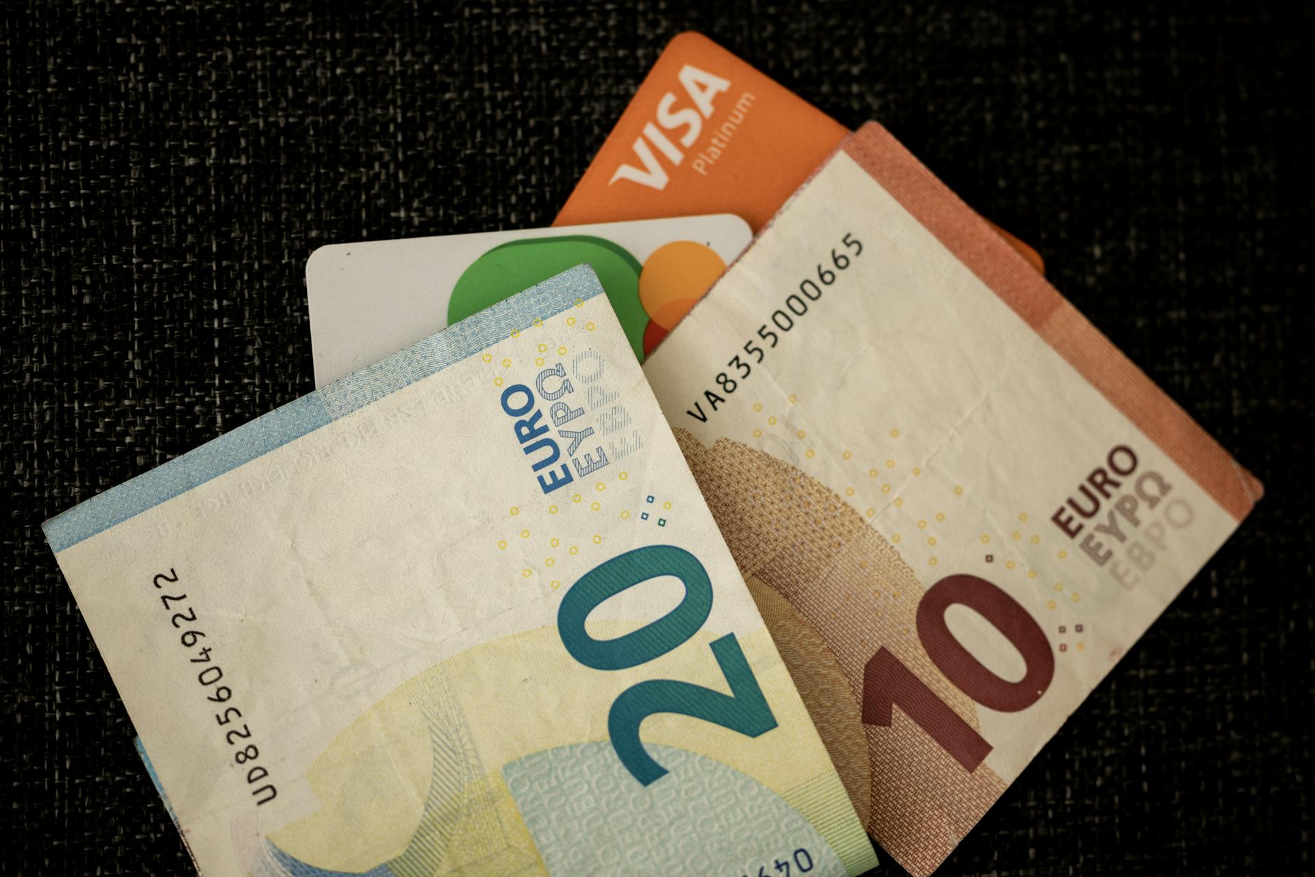 Close-up of euro banknotes and credit cards on a dark textured surface.