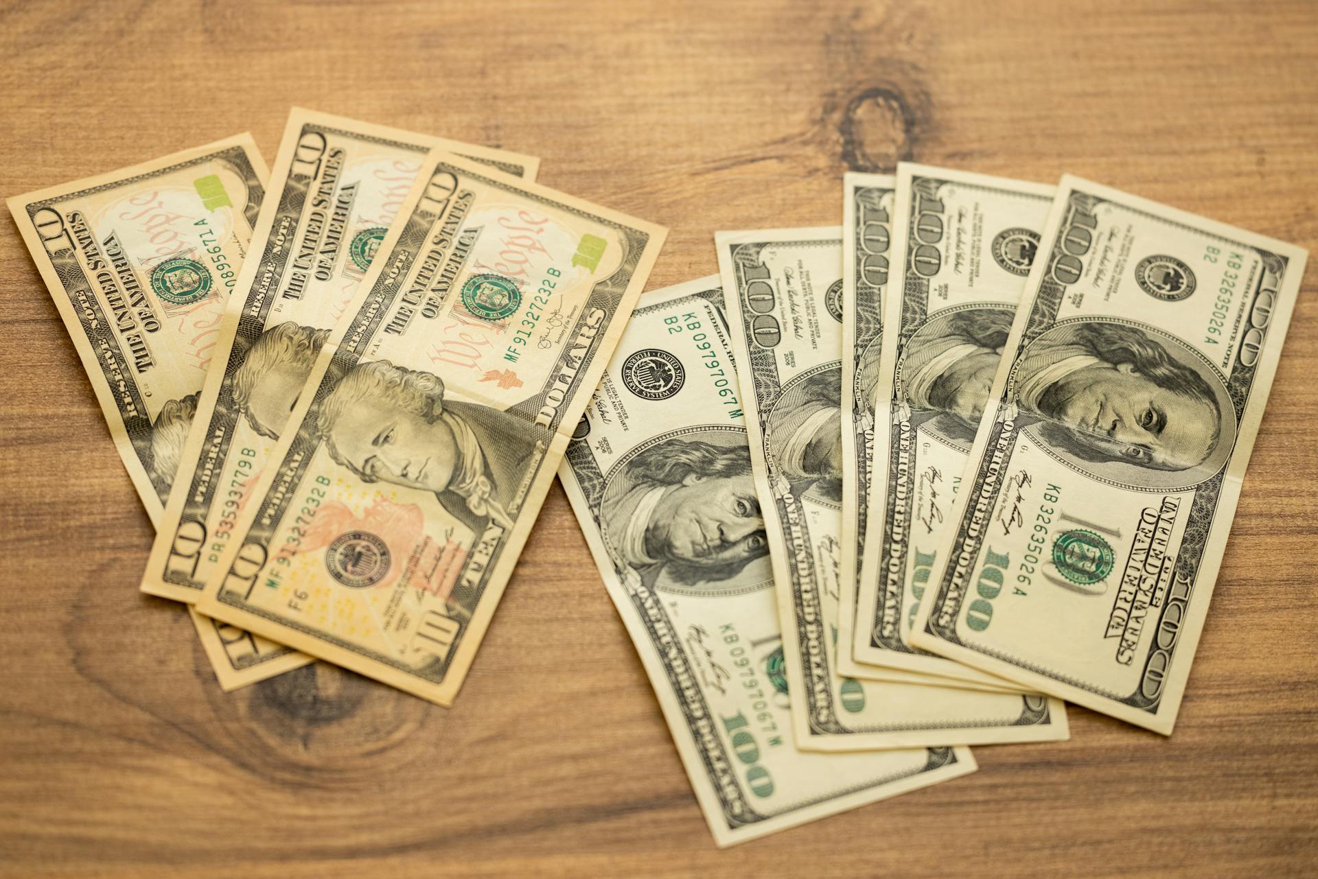 A collection of US dollar bills arranged on a wooden surface, showcasing currency denominations.