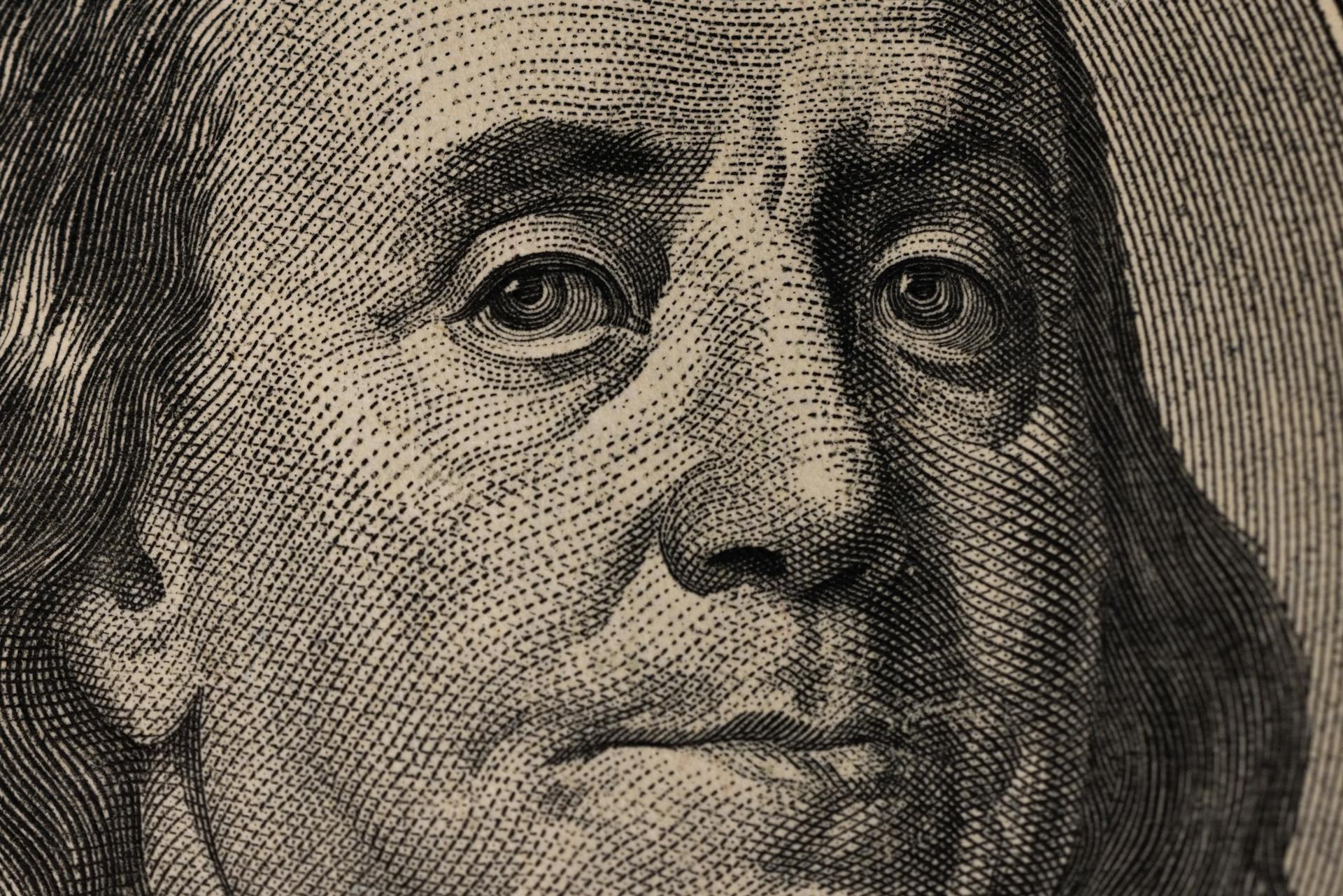 Detailed view of Benjamin Franklin's face on a US dollar bill, showcasing fine engraving.