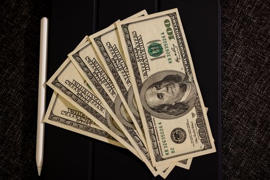 Photo by Engin Akyurt Spread of US dollar bills on black surface with stylus, symbolizing finance and technology.