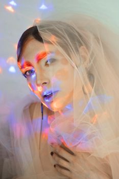 Mesmerizing portrait of a model draped in a sheer veil, highlighted by colorful light patterns.