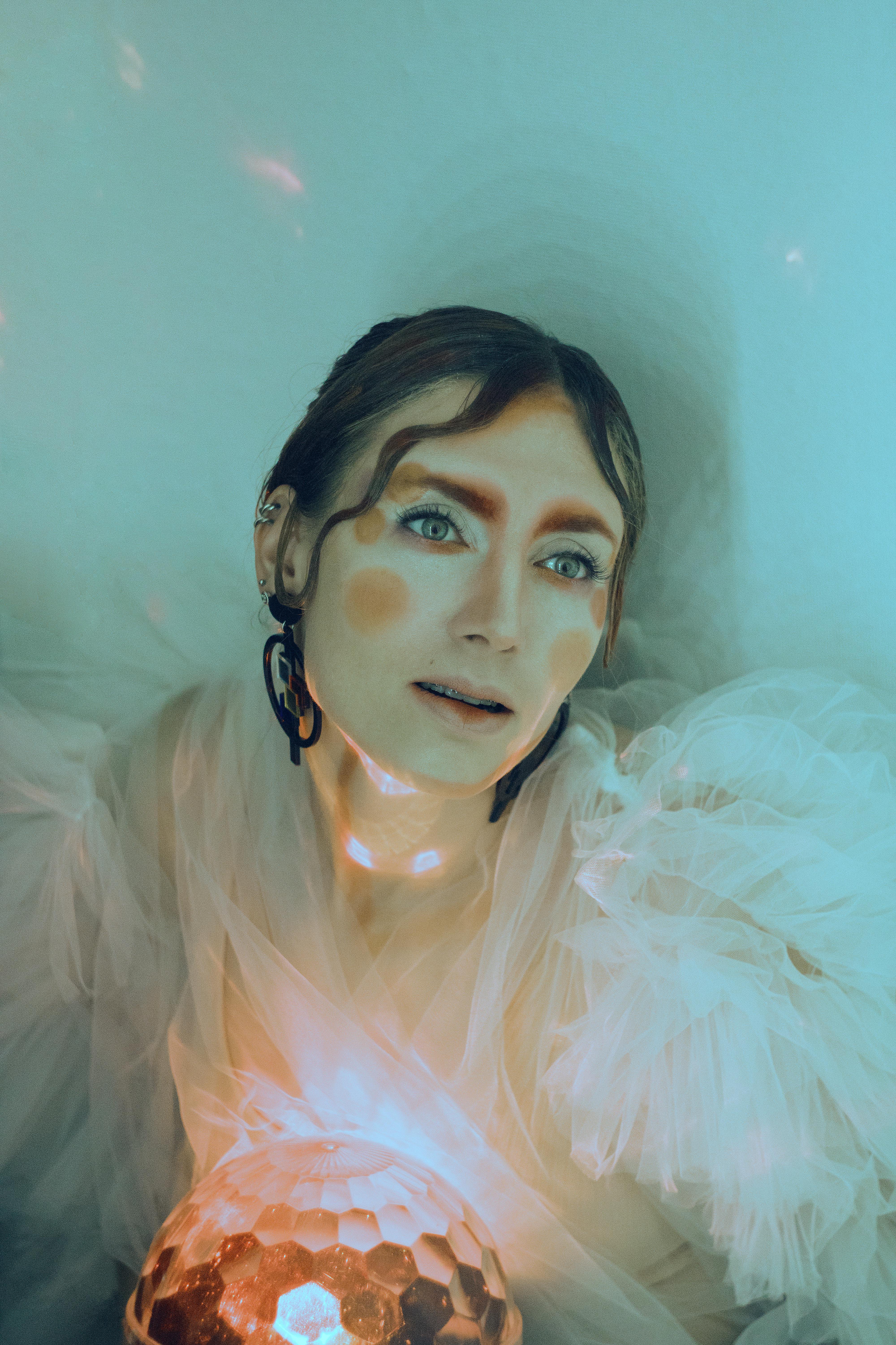 Ethereal portrait of woman with artistic face paint and luminous sphere in dreamy setting.