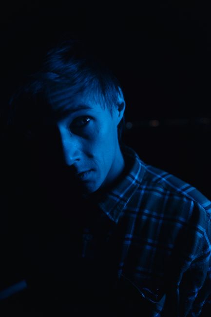 Mysterious portrait of a man partially illuminated by blue light, wearing a plaid shirt.