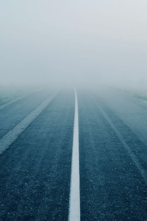 Free A foggy deserted road disappearing into thick mist, conveying a sense of mystery. Stock Photo