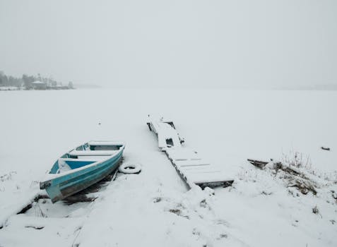 A tranquil winter scene with a snow-covered boat resting on a frozen lake alongside a pier.