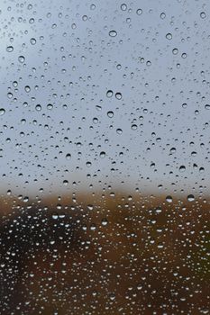 Close-up of raindrops on glass, forming an abstract pattern against a blurred outdoor background.