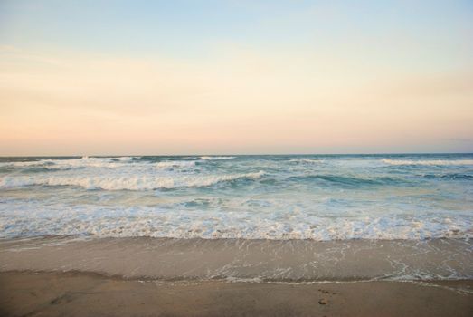 Serene shoreline with gentle waves under a pastel sunset, perfect for peaceful nature settings.