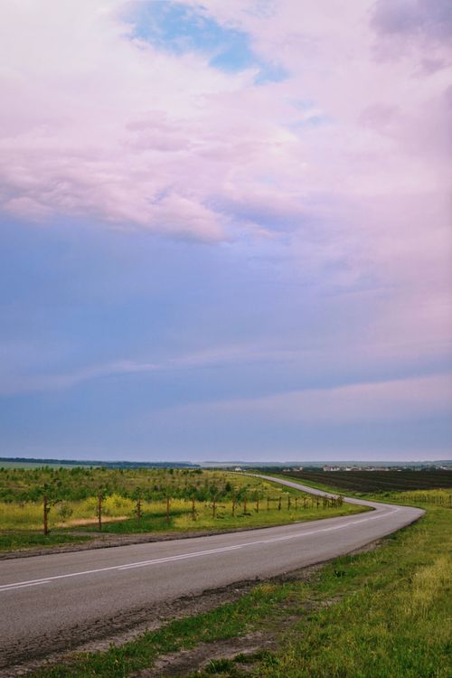 Free Winding rural road through open countryside under a dramatic sky, ideal for travel themes. Stock Photo