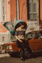 Man in Black Jacket and Black Pants Sitting on Red Car