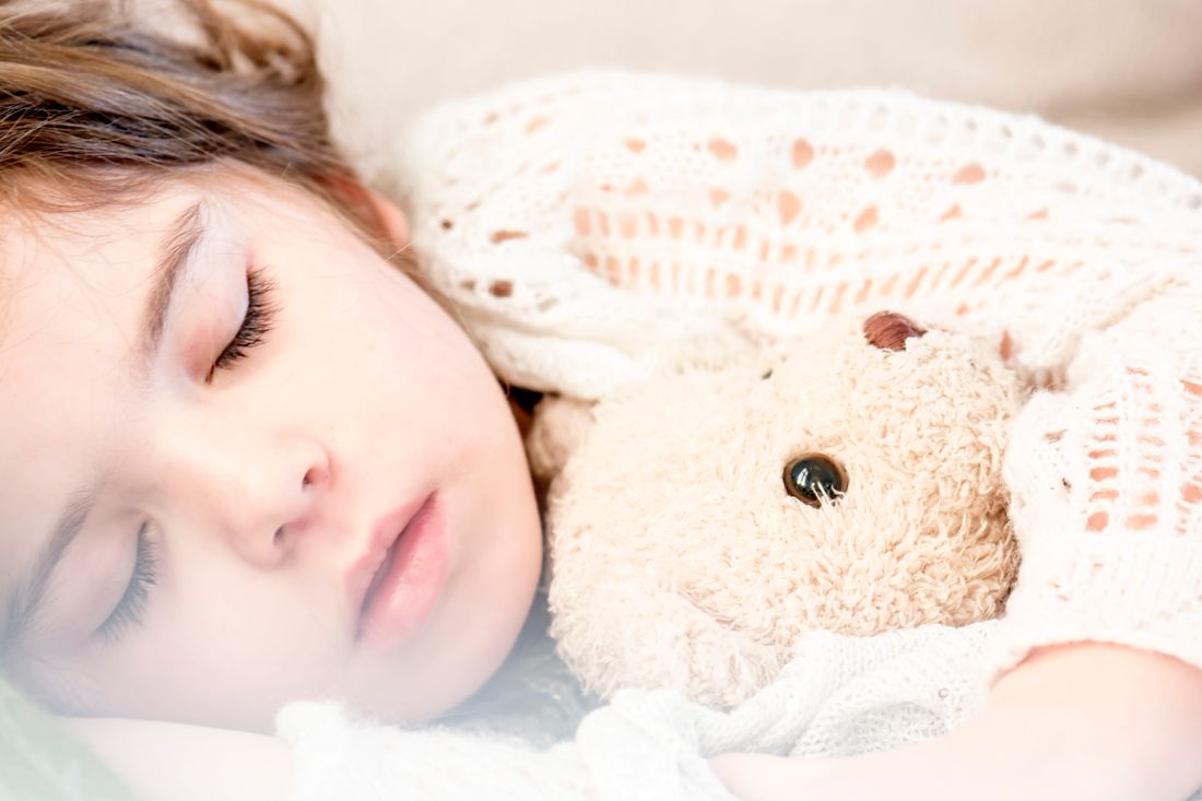 A young child sleeping with a teddy bear