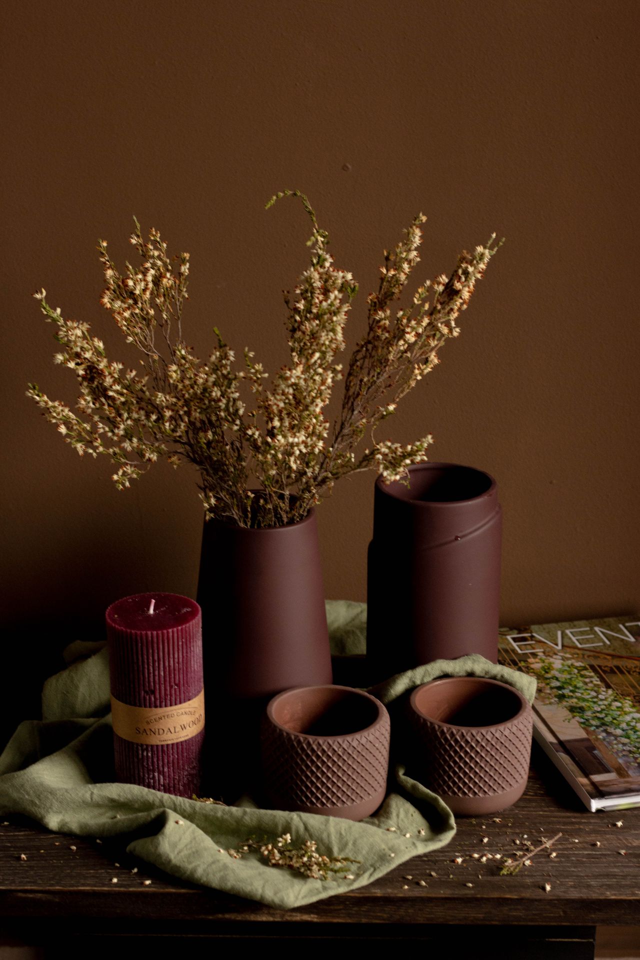 Brown ceramic vases and a red candle with dried flowers on a wooden table