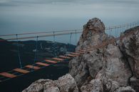 Dramatic view of a hanging bridge over rugged mountains with distant sea horizon.