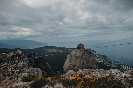 Explore the dramatic coastal landscape with a footbridge and expansive sea view, captured under a moody sky.