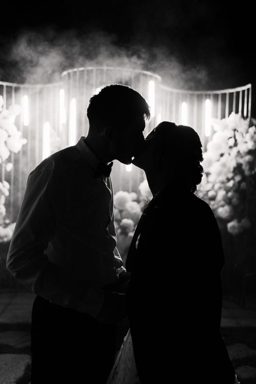 Free A beautiful black and white silhouette of a couple kissing, surrounded by lights. Stock Photo