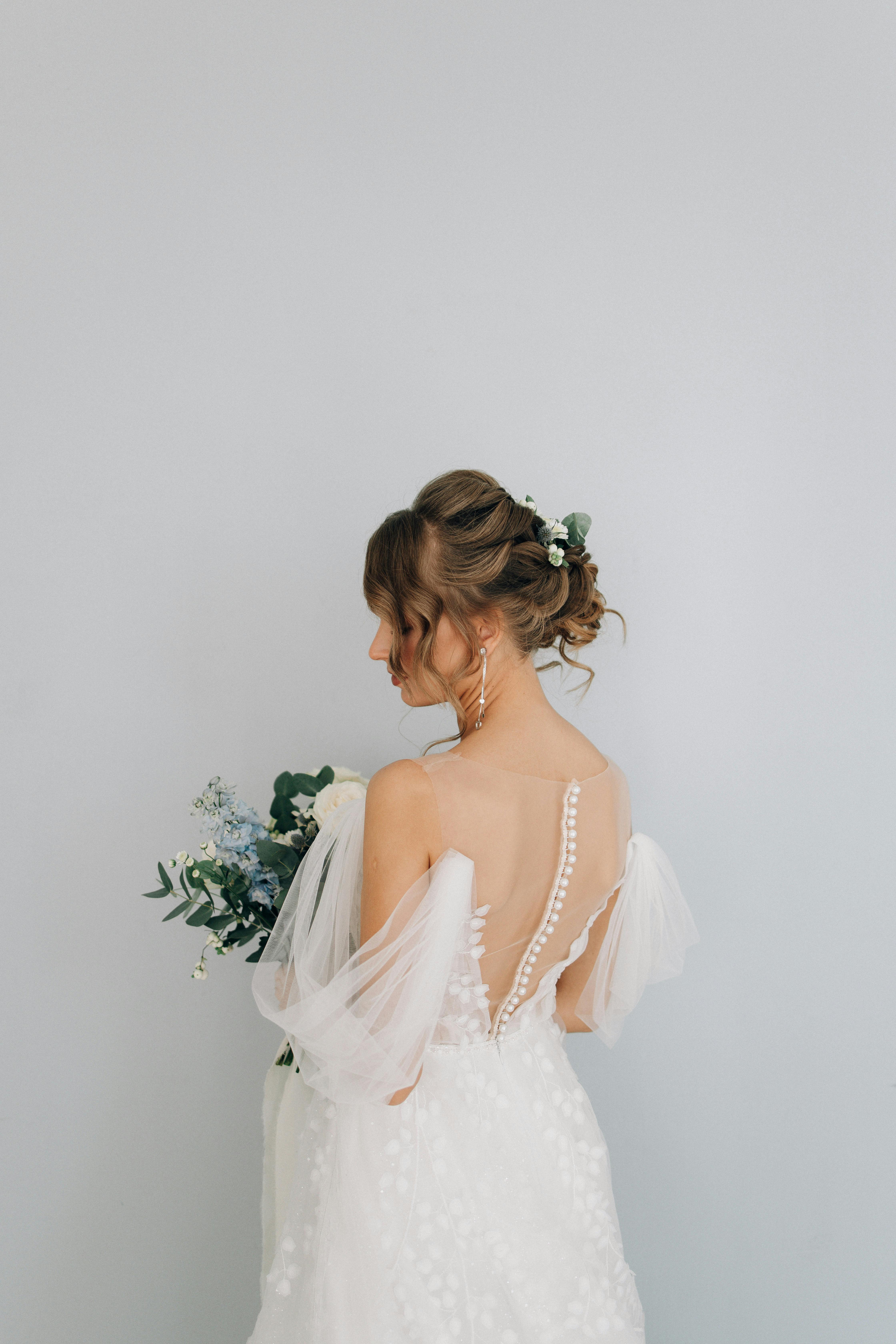 Elegant back view of a bride in a wedding dress holding a bouquet against a soft background.