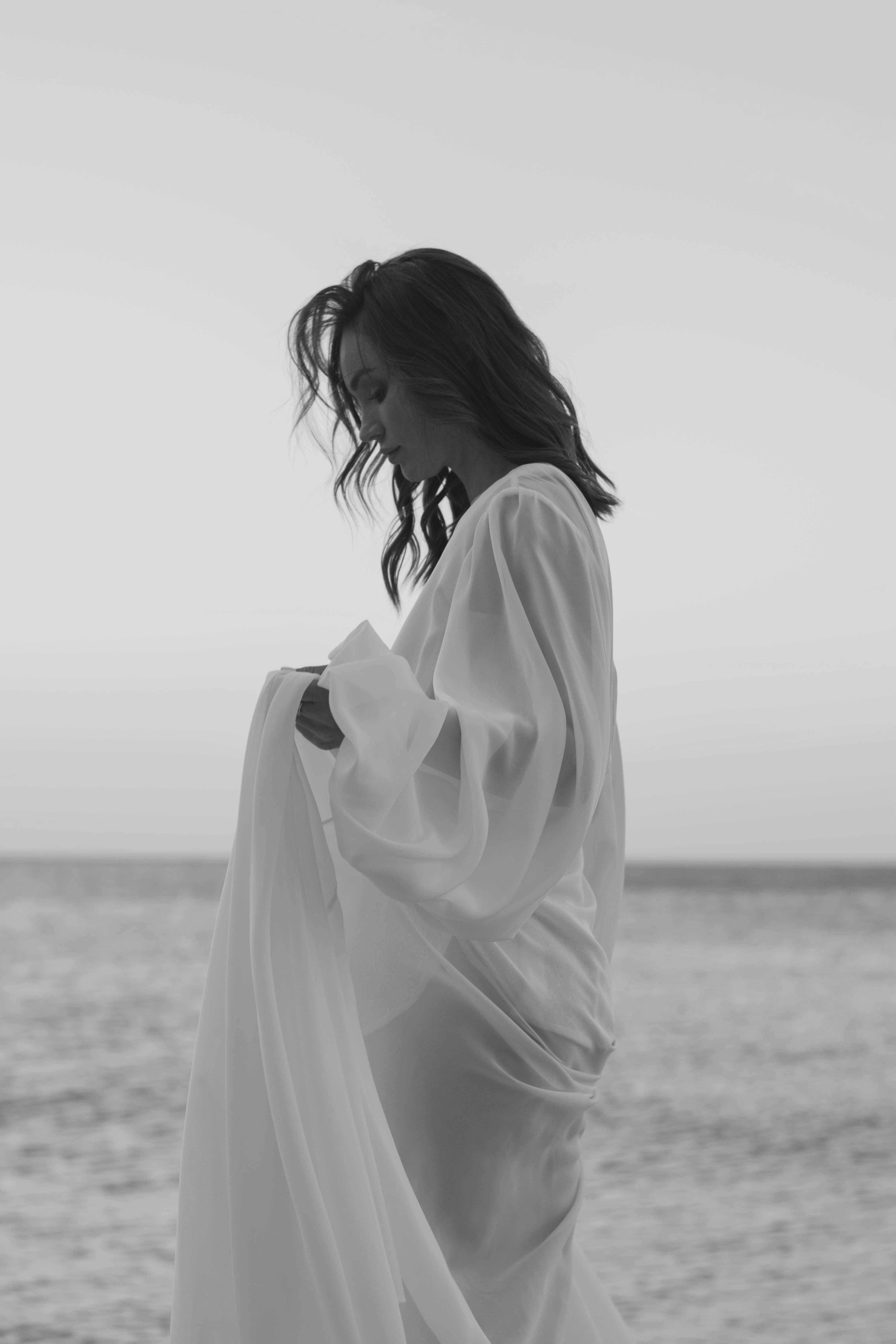 优雅的女人穿着飘逸的连衣裙，眺望大海，散发着宁静的气息