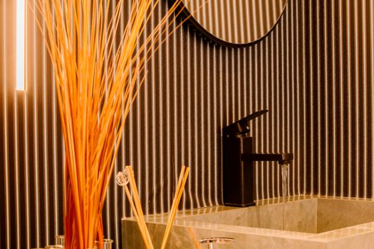 Modern bathroom interior with sleek faucet, striped wall, and decorative reed sticks.