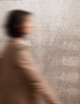 Artistic shot of a person walking, displaying motion blur against a textured wall.