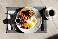 桌子上摆着美味的早餐，有鸡蛋、培根、水果和咖啡，阳光明媚