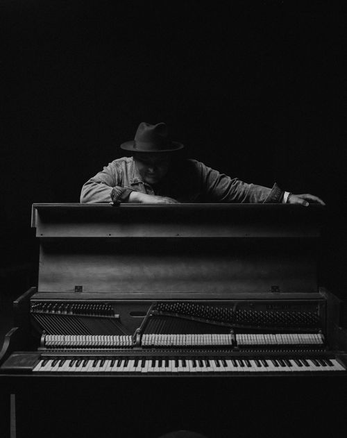Free A man in a fedora playing a piano in a dramatic black and white portrait. Stock Photo