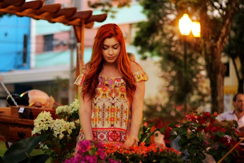 Red-Haired Woman in Floral Dress Looking at the Flowers