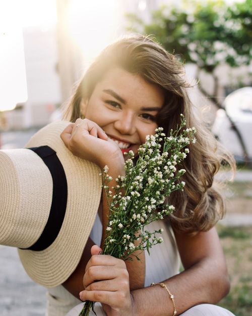Free A smiling woman holding flowers enjoys a sunny day outdoors, exuding happiness and warmth. Stock Photo