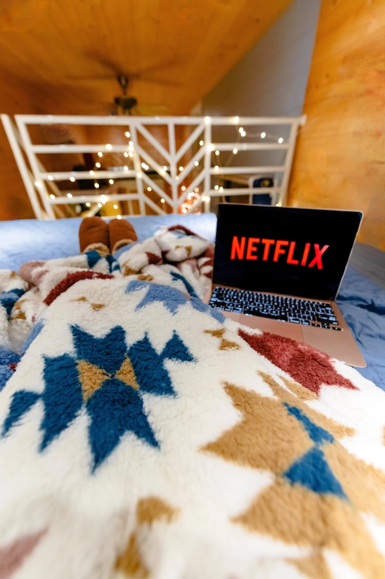 A Person Lying On The Bed Covered With Blanket In Front Of A Laptop