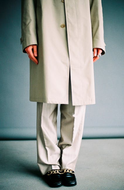 Stylish studio photo of a person in a beige trench coat and pants with chain loafers, exuding elegance.
