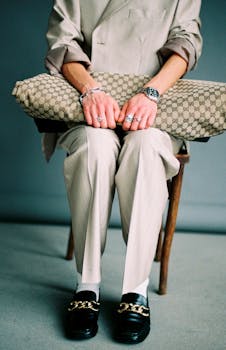 Stylish man in beige suit and loafers holding a designer bag, showcasing luxury fashion accessories.