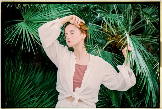 Woman with Closed Eyes Touching a Leaf of a Palm
