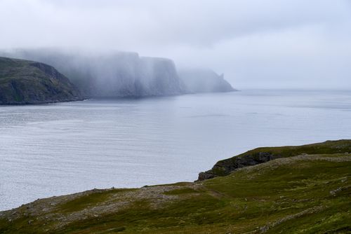 Cliffs wrapped in fog above still water, photo by Barnabas Davoti on Pexels