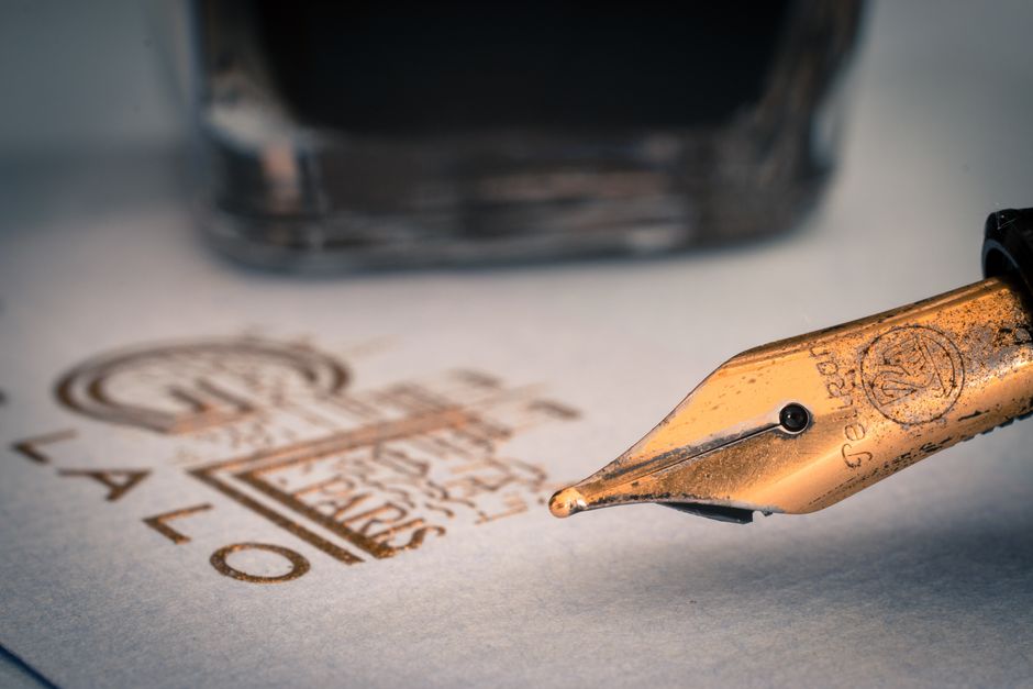 A handwritten signature next to an engraved silver pendant A handwritten signature next to an engraved silver pendant